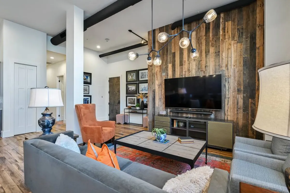 A warm and welcoming living room accented by a wood-paneled wall, comfortable seating, modern lighting, and a television. The inviting atmosphere encourages cozy evenings, entertaining guests, and quiet afternoons.