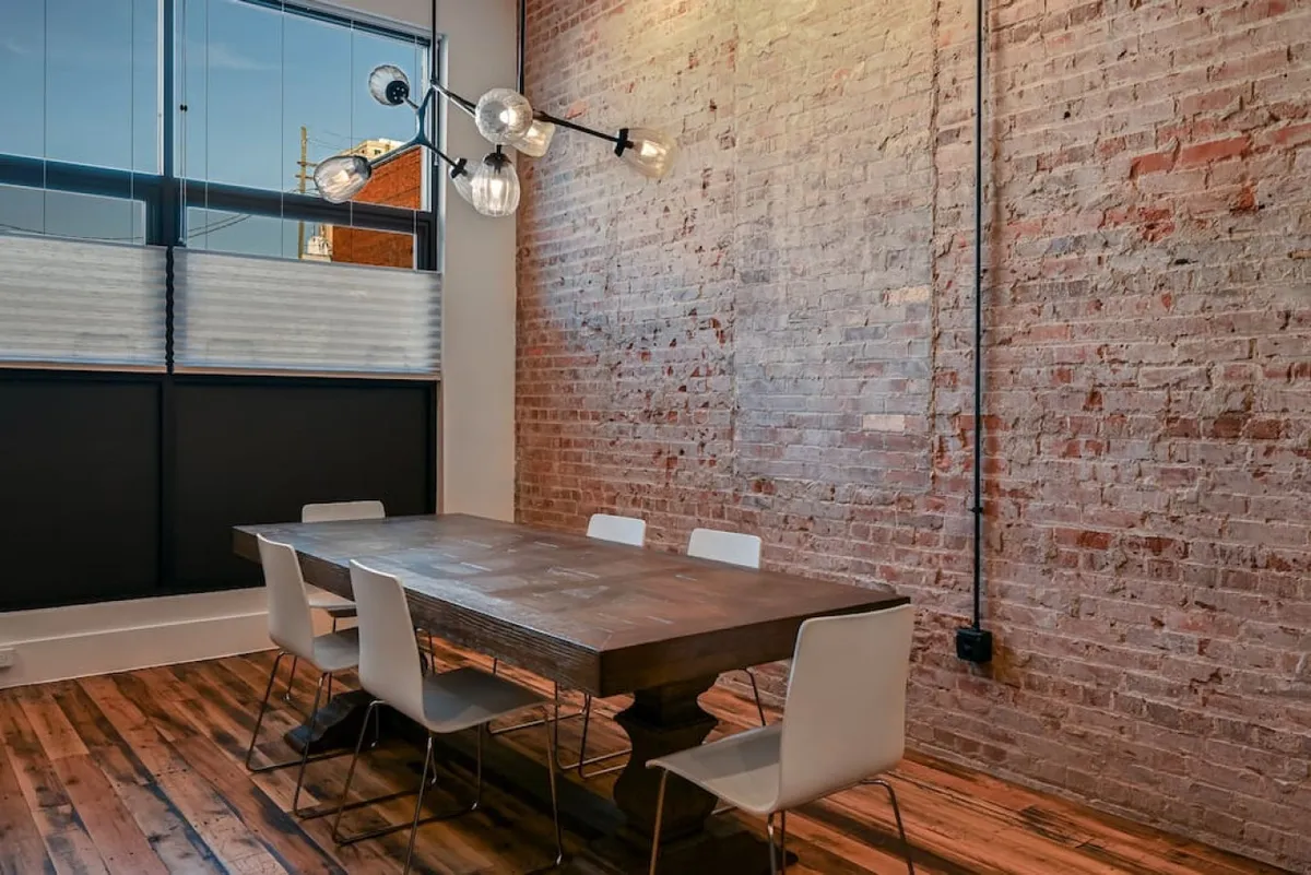 This image features an intimate wooden dining table set beneath a unique chandelier, framed by an exposed brick wall. The scene puts focus on the dining experience, suggesting a cozy spot for lingering over meals or spirited conversation.