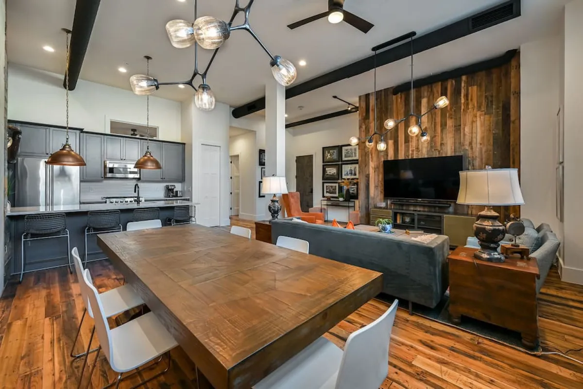 A warm and welcoming open-concept space with a dining table, wood accent wall, comfortable seating area, and stylish lighting. The layout encourages gatherings and easy flow, echoing the friendly, social atmosphere described in the section.